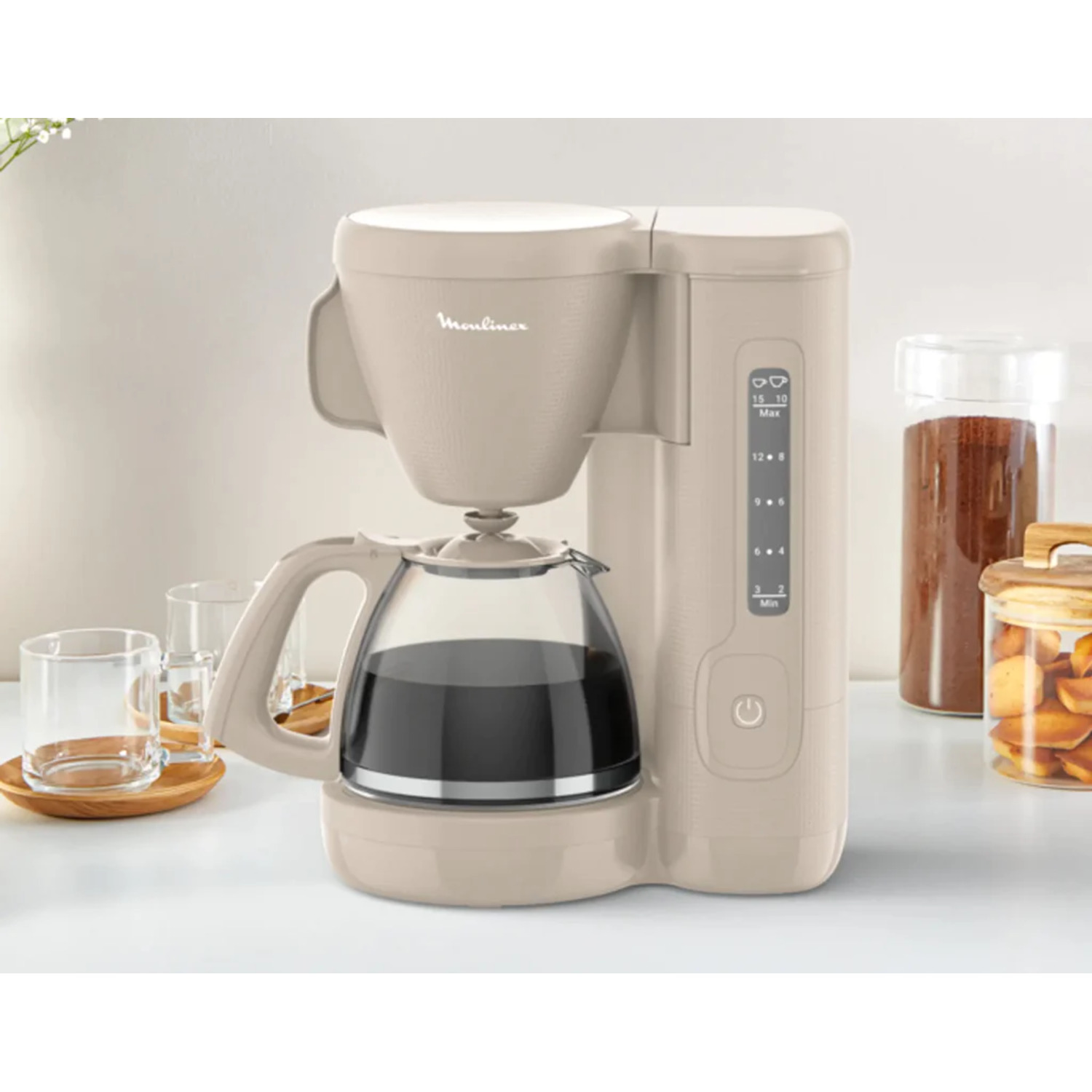 A beige Moulinex coffee maker with a glass carafe, filled with coffee. Clear glasses and jars of coffee and cookies are present.