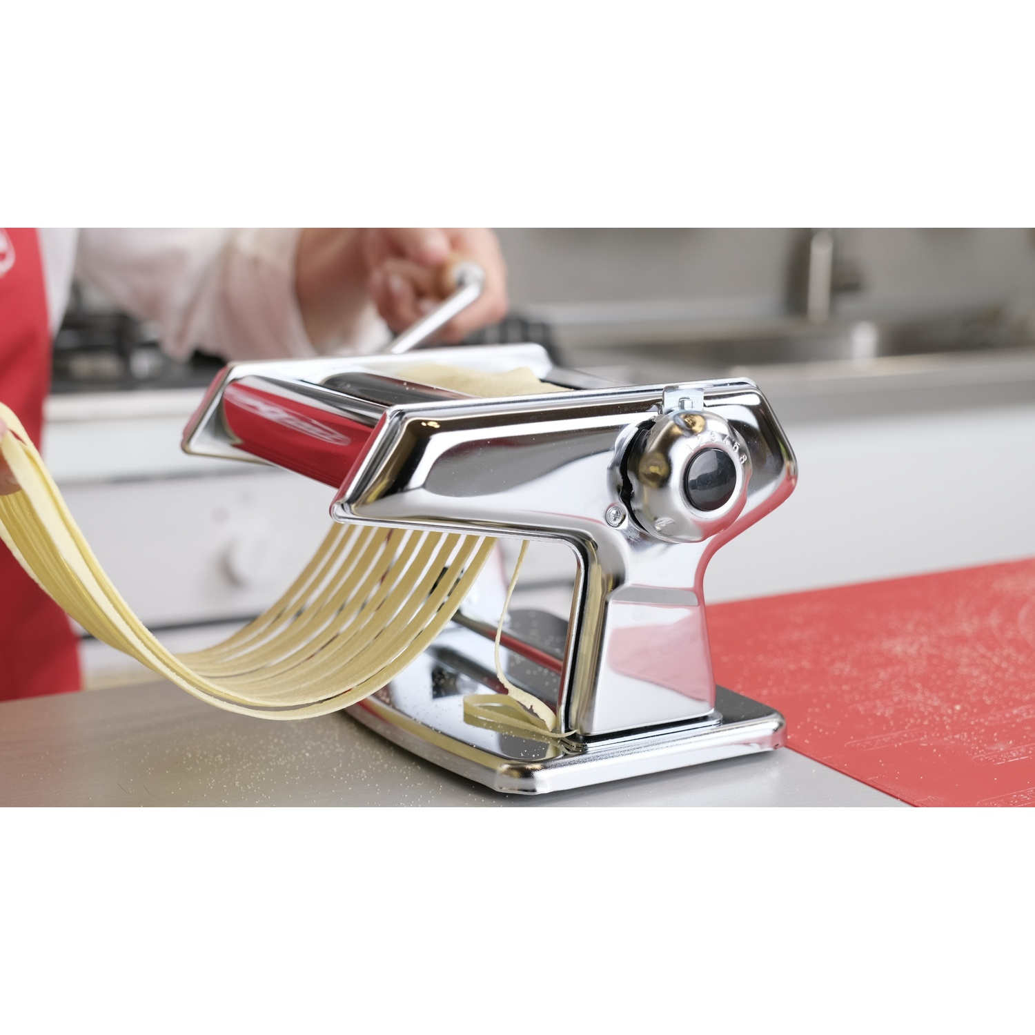 Una macchina per la pasta sta facendo spaghetti lunghi e sottili. Sono visibili le mani di una persona.
