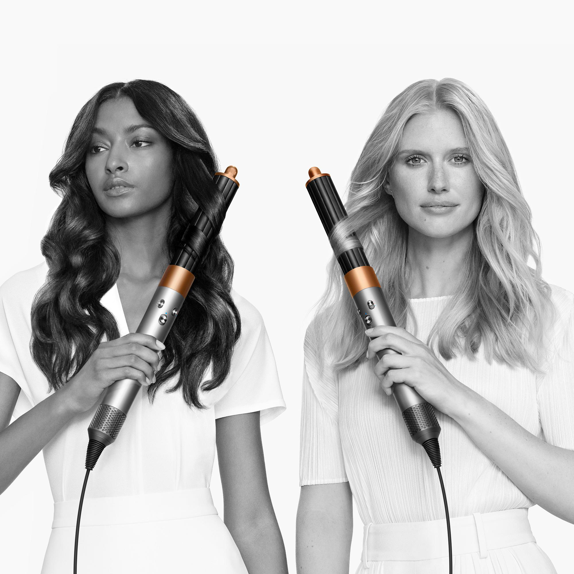 Zwei Frauen, eine mit dunklem Haar, die andere mit blondem, halten jeweils einen Haarstyler. Beide tragen Weiß, mit weißem Hintergrund.