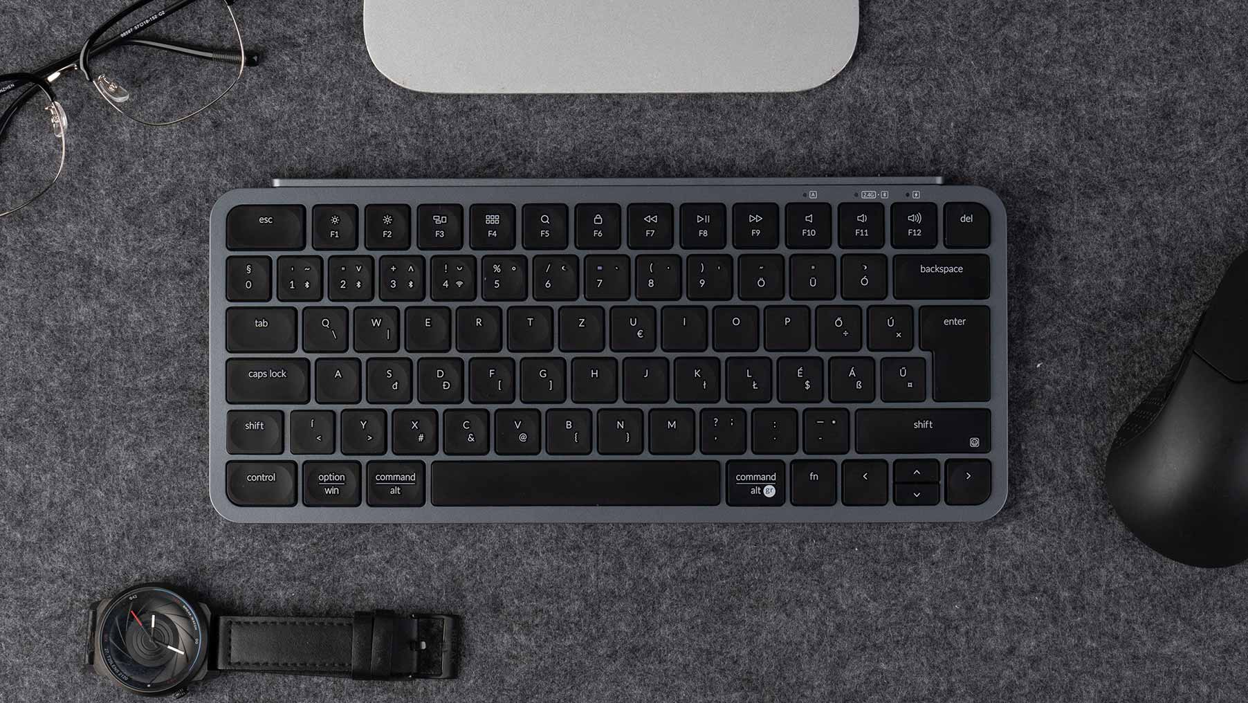 Draufsicht auf eine graue Tastatur, Maus und Uhr auf einer grauen Oberfläche.