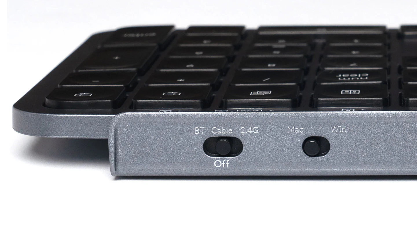 Nahaufnahme einer silbernen Tastatur mit schwarzen Tasten. Sie hat einen BT/Kabel-Schalter und einen Mac/Win-Schalter. Die Tasten sind im Fokus.