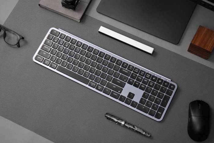 Draufsicht auf einen Schreibtisch mit Tastatur, Maus, Stift, Brille, Laptop und anderen Büromaterialien.