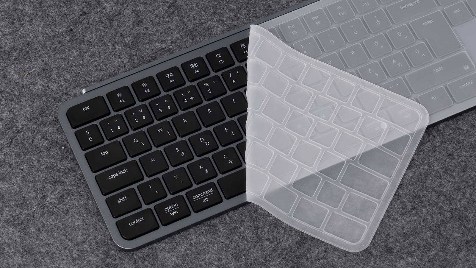 Eine Tastatur mit transparentem Bezug liegt auf einer grauen Oberfläche. Die Tastatur ist schwarz mit weißen Zeichen. Der Bezug ist transparent.
