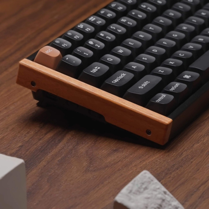 Nahaufnahme einer schwarzen Tastatur mit Holzrahmen. Die Tasten sind schwarz mit weißen Buchstaben. Eine orangefarbene "esc"-Taste ist sichtbar.