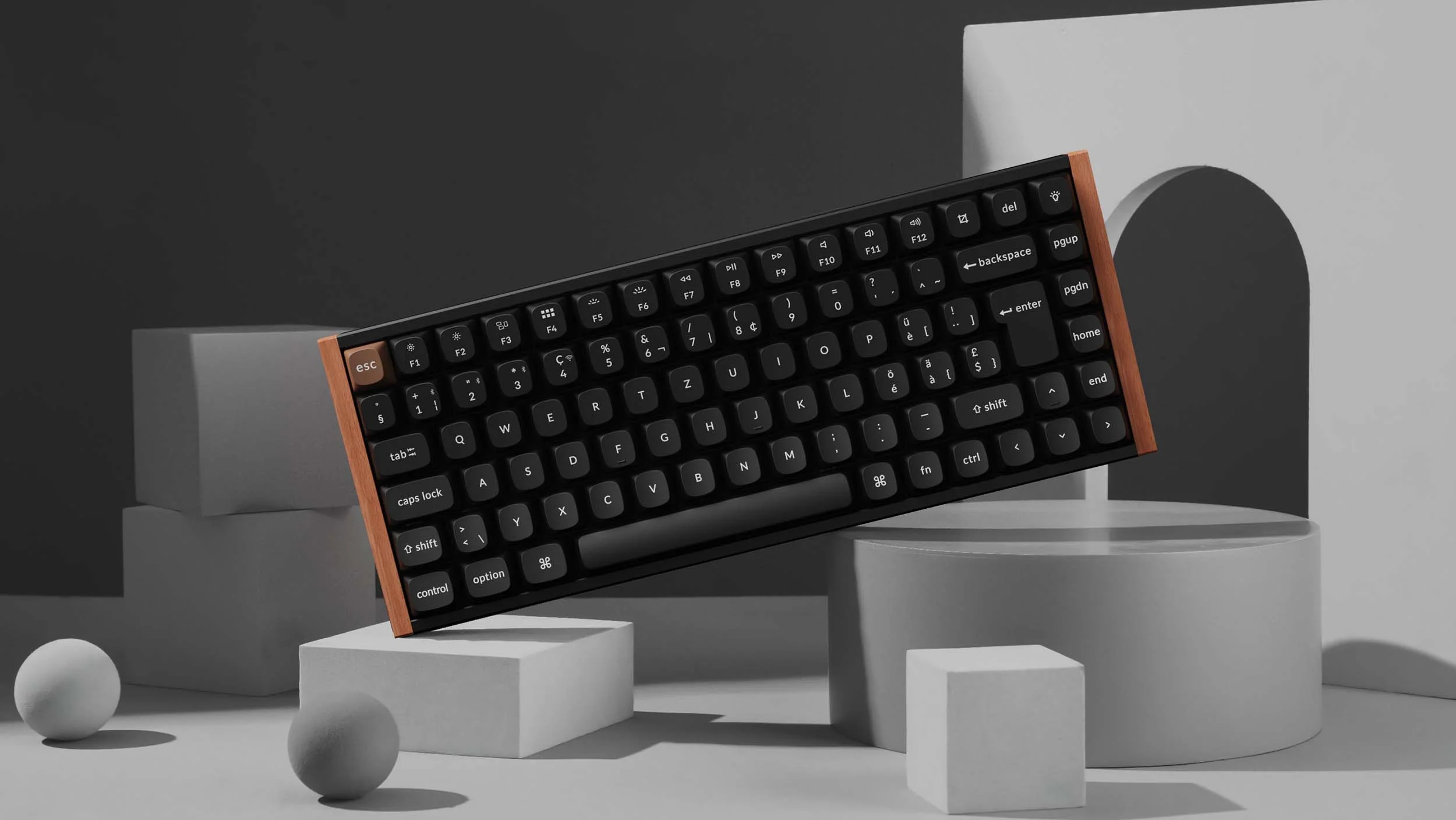 Eine schwarze Tastatur mit Holzrahmen liegt auf geometrischen Formen. Der Hintergrund ist grau.