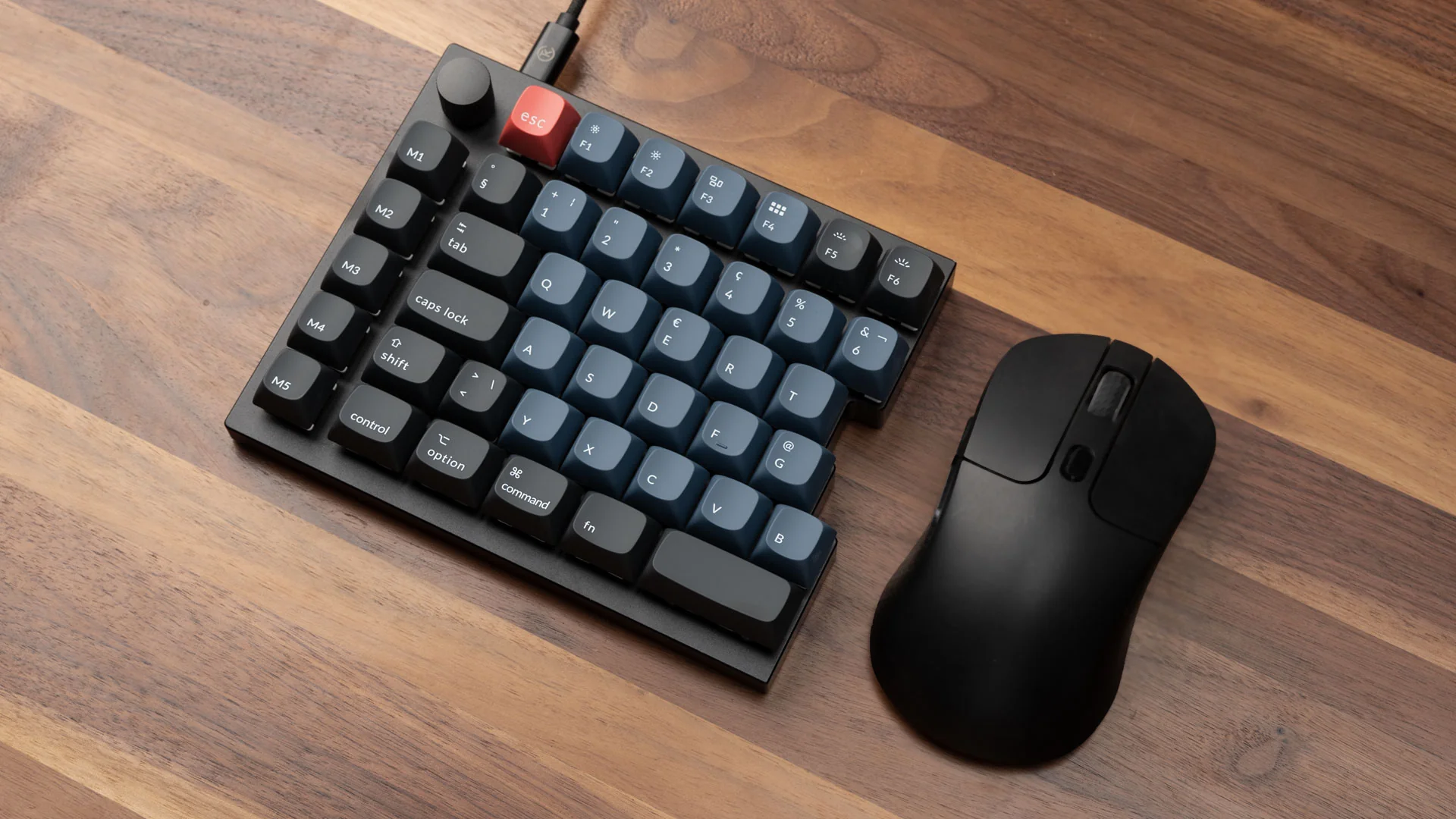 Eine schwarze Tastatur mit blauen Tasten, eine schwarze Maus und ein Kabel auf einer Holzoberfläche. Die Tastatur hat eine rote Escape-Taste.