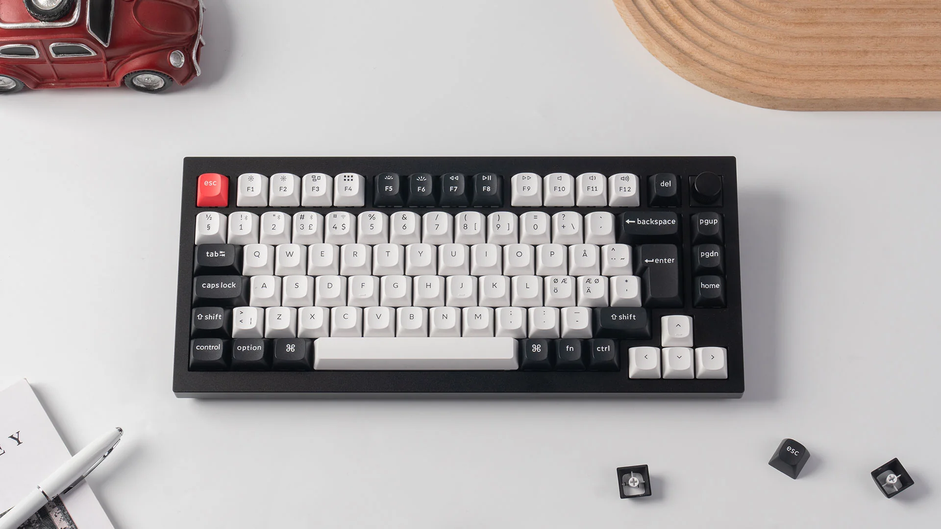 Schwarze und weiße mechanische Tastatur auf weißer Oberfläche mit einem roten Spielzeugauto oben links.