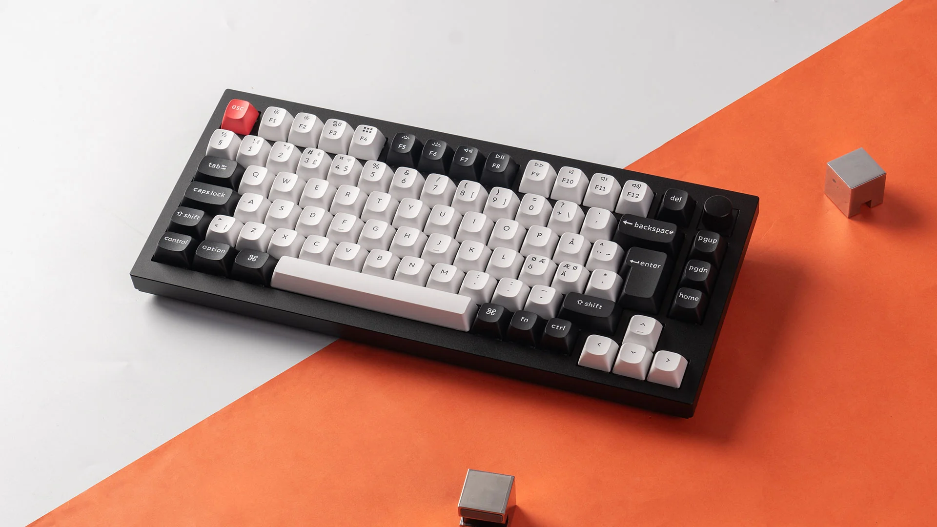 Eine schwarz-weiße mechanische Tastatur auf orange-weißem Hintergrund, mit zwei kleinen Metallwürfeln.