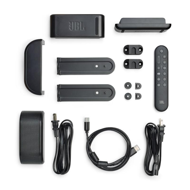 Draufsicht auf JBL Soundbar-Komponenten. Beinhaltet Soundbar, Fernbedienung, Halterungen, Kabel und Netzteile, alles schwarz, auf Weiß angeordnet.