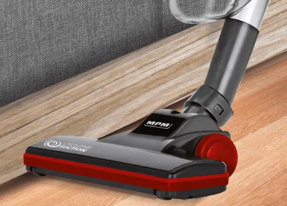 Zbliżenie czarnej i czerwonej głowicy odkurzacza na drewnianej podłodze. Szara tapicerowana powierzchnia w tle.