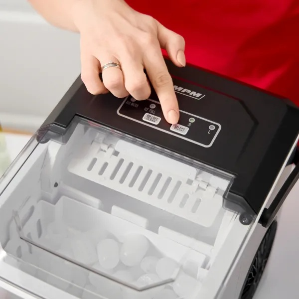 Ręka naciska przycisk 'SELECT' na czarnej maszynie do lodu. Maszyna jest otwarta, pokazując kostki lodu. Czerwona koszula w tle.