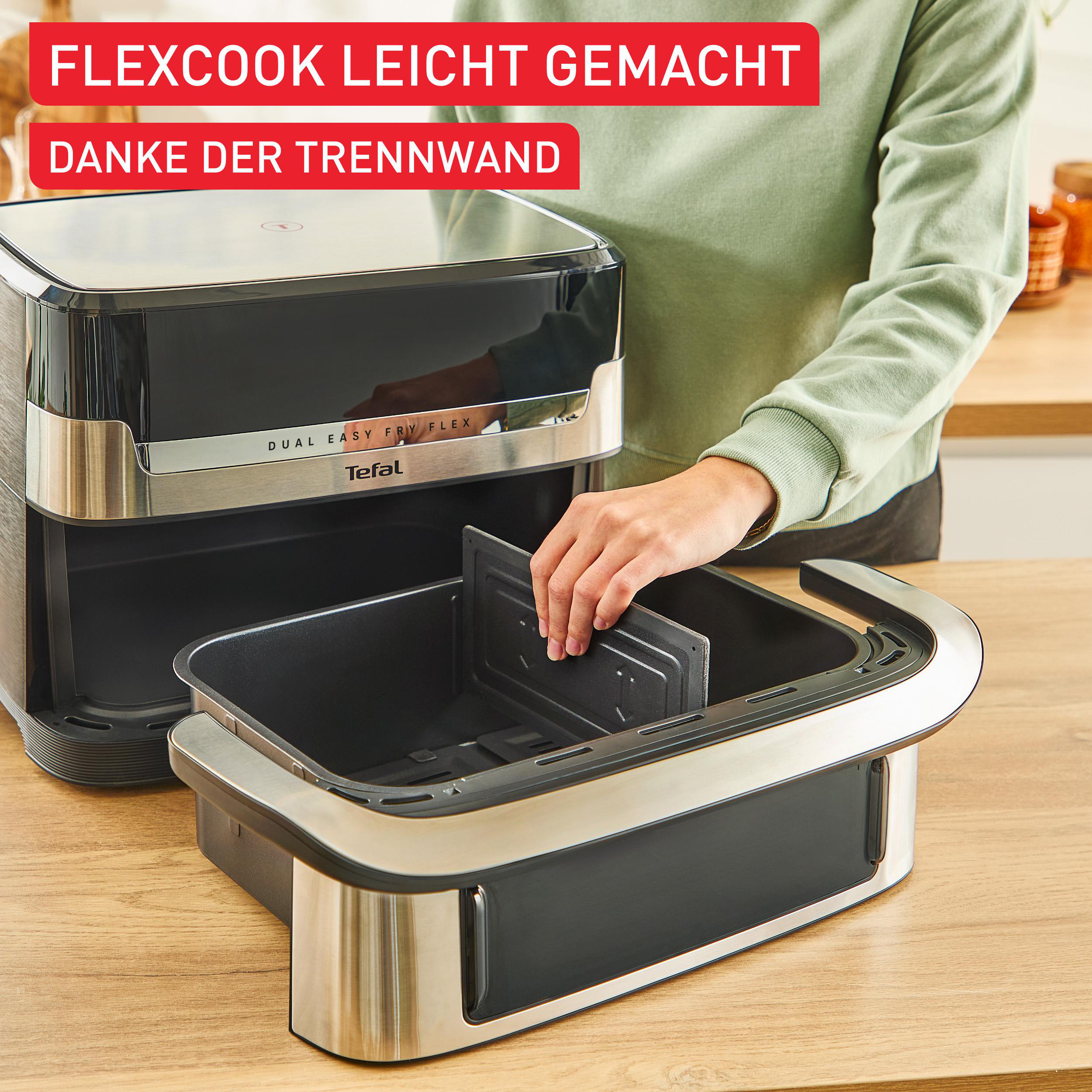 Eine Person setzt einen Teiler in eine schwarze Heißluftfritteuse ein. Die Heißluftfritteuse steht auf einem Holztisch, mit Text darüber.