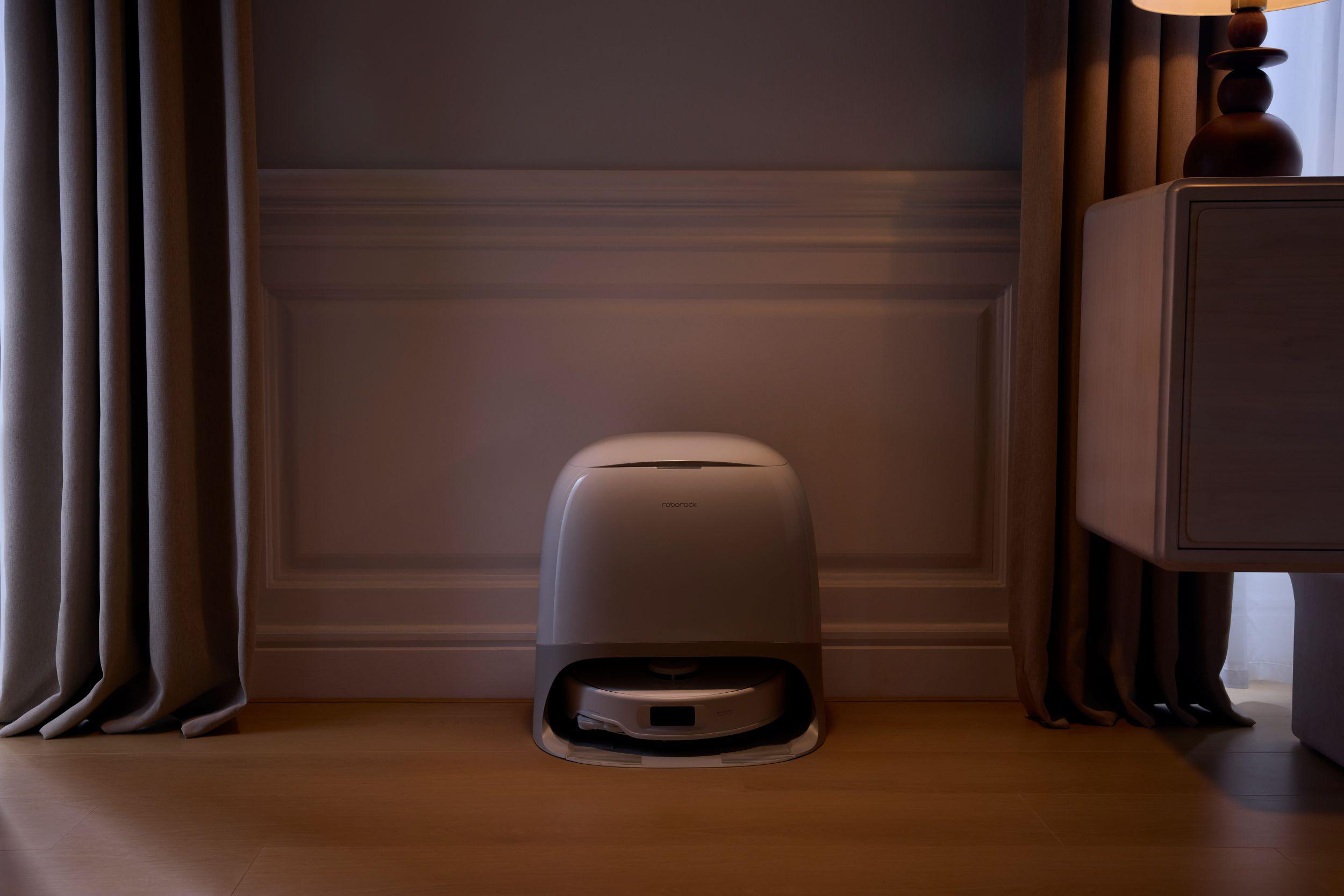Ein Roboter-Staubsauger steht auf einem Holzboden. Vorhänge umrahmen die Szene, rechts ein Schrank.