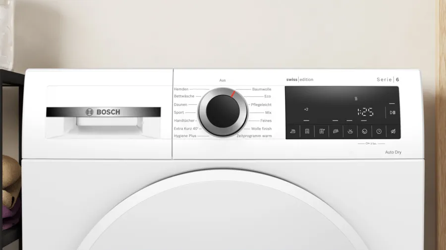 Un sèche-linge blanc Bosch Serie 6. Il possède un panneau de commande avec un cadran et un affichage numérique indiquant 1:25. Le sèche-linge est sur un mur clair.