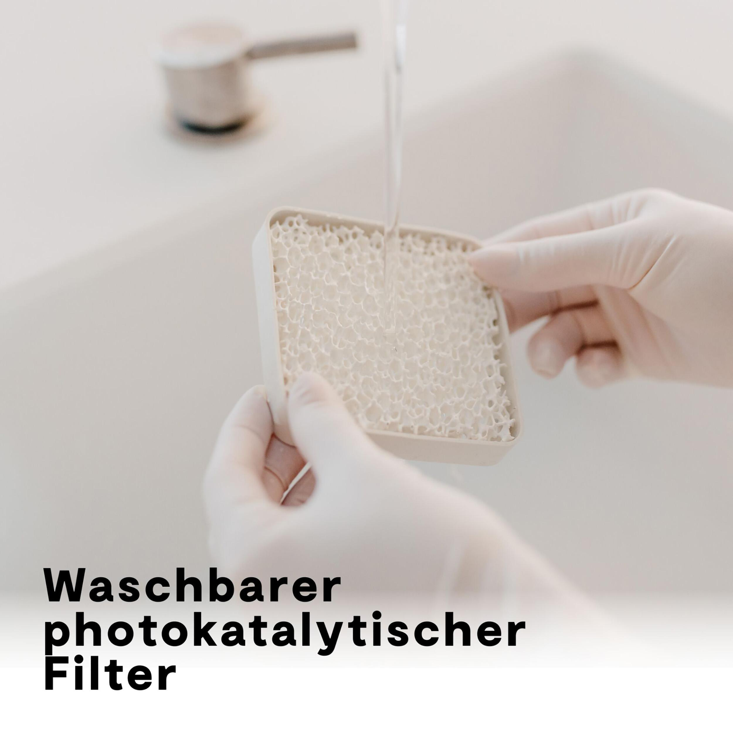 Hände in Handschuhen halten einen Filter. Wasser fließt aus einem Wasserhahn auf den Filter. Text unten: waschbarer photokatalytischer Filter.