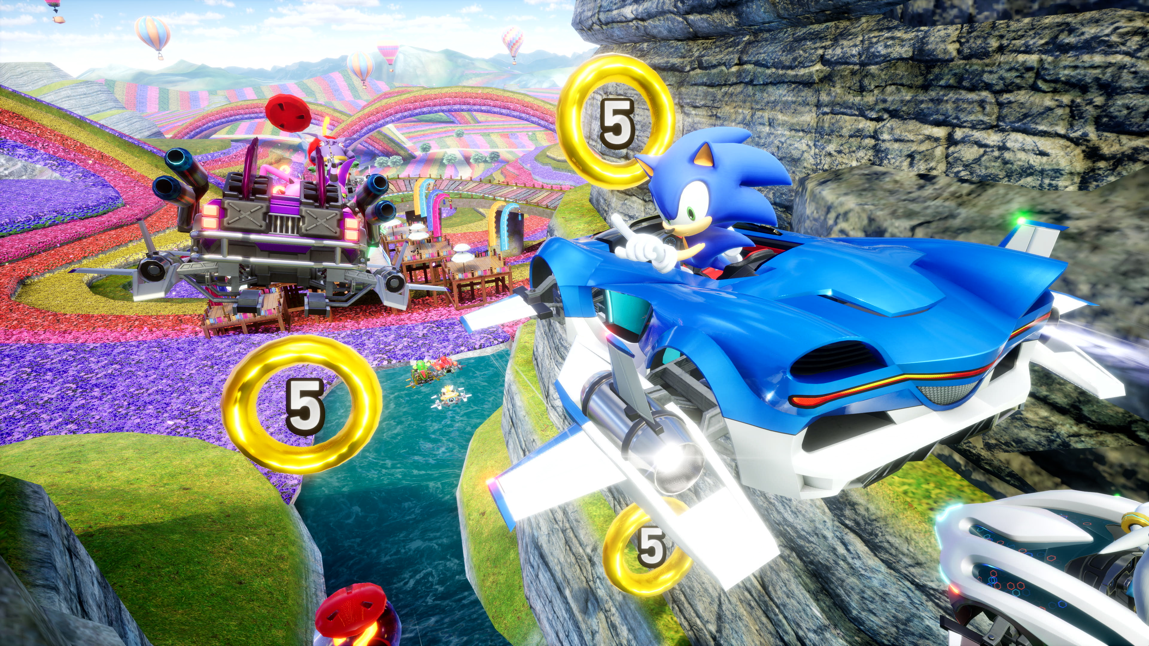 Sonic dans une voiture bleue vole devant des anneaux dorés, un paysage coloré en arrière-plan. Une falaise rocheuse est à droite.
