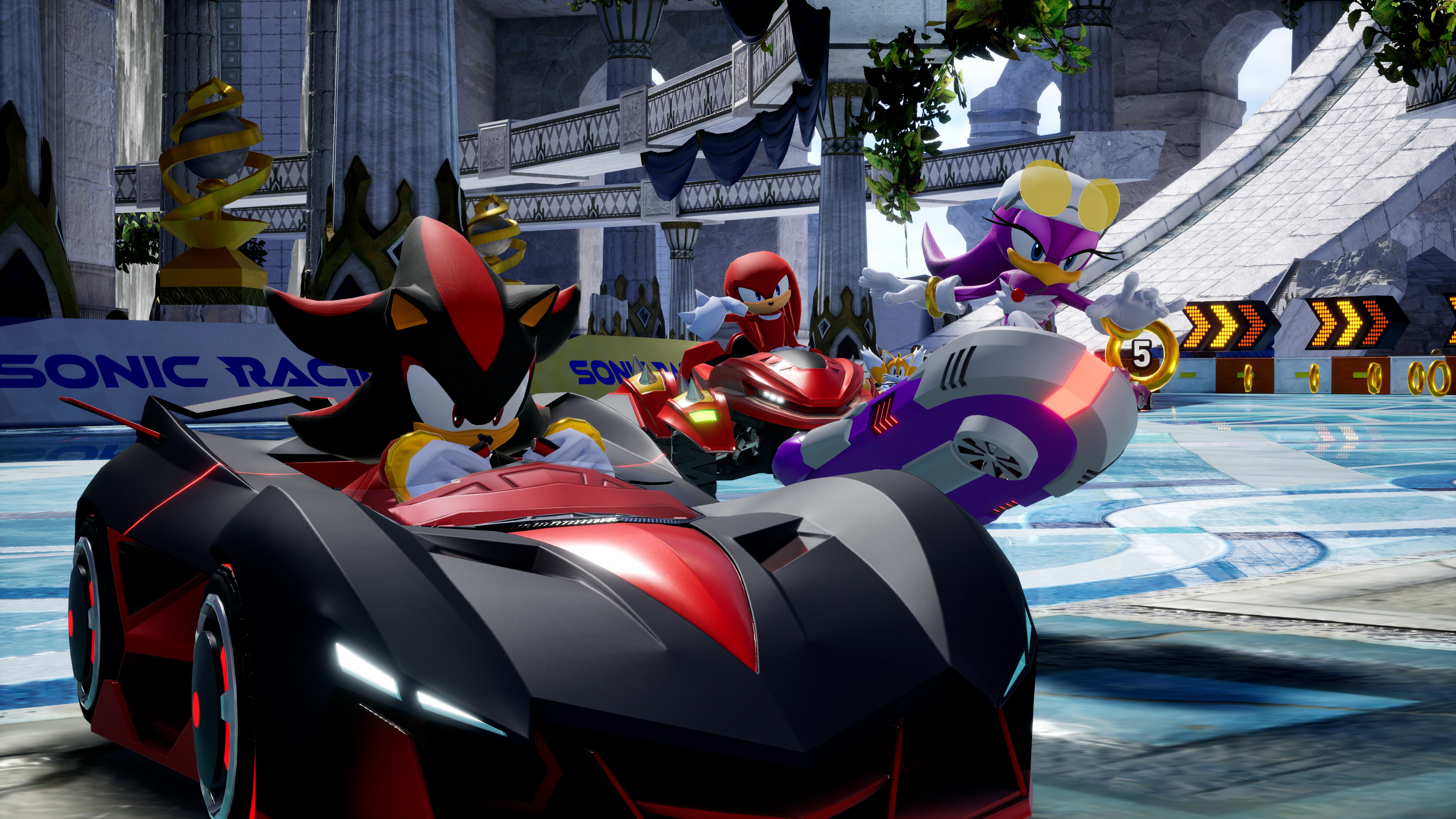 Shadow, Knuckles et Wave courent dans leurs véhicules dans un jeu de course Sonic. La piste a une surface bleue et des anneaux dorés.