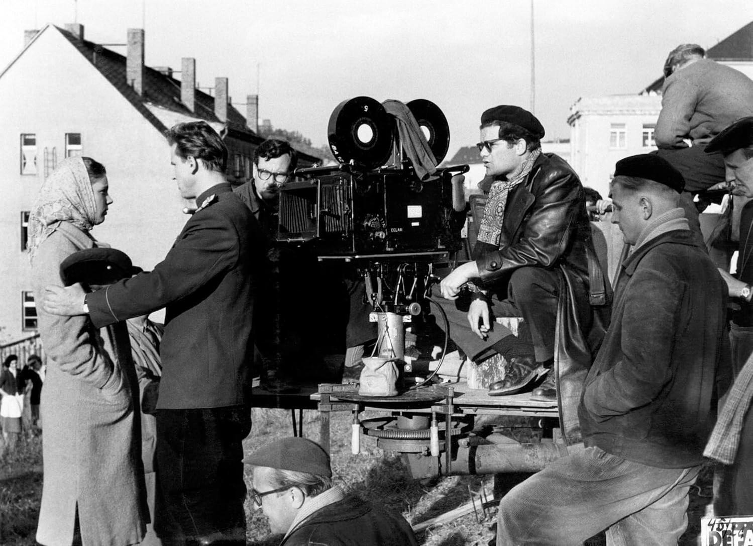 Filmszene. Schauspieler in Kostümen, Kamerateam und Ausrüstung. Gebäude im Hintergrund. Schwarz-Weiß-Bild.