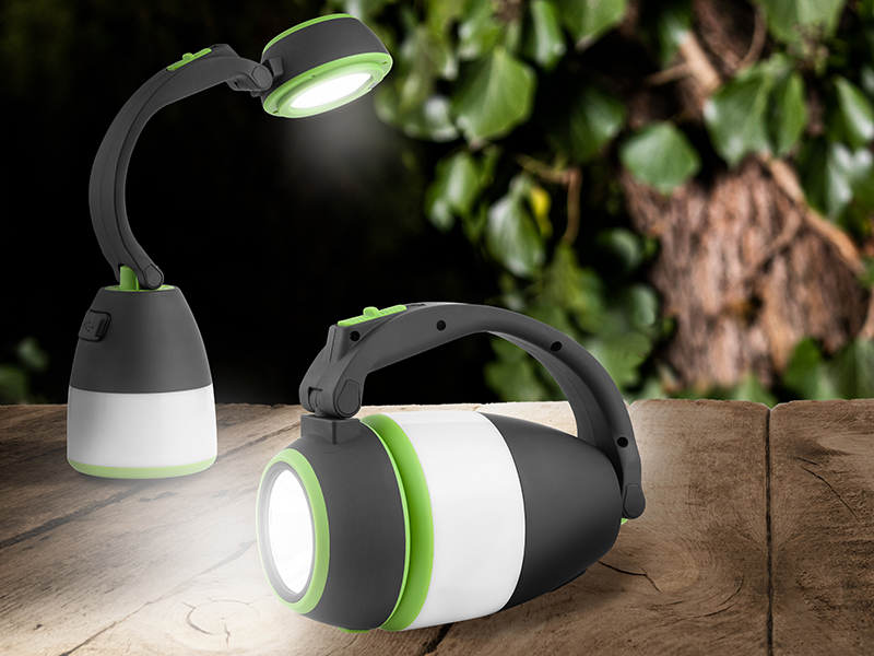 Dwie czarne, białe i zielone lampy LED. Jedna to lampa, druga to latarka. Znajdują się na drewnianej powierzchni z rozmytym zielonym tłem.