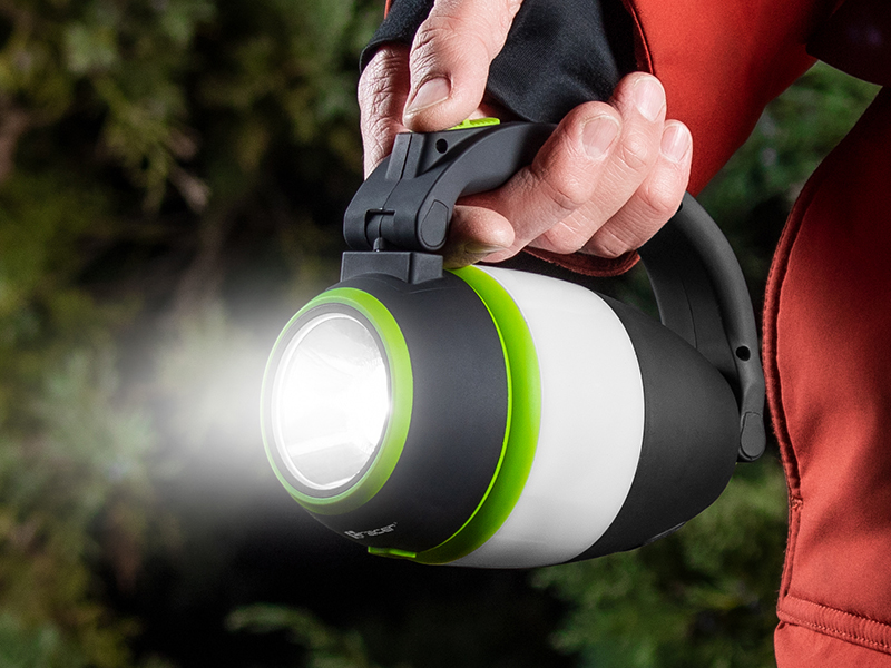 Osoba trzyma czarno-zieloną latarkę, która emituje jasną wiązkę światła. W tle widać rozmyte zielone liście.
