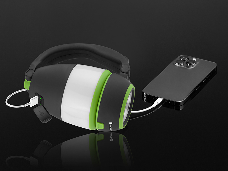 Czarno-zielona latarnia ładuje smartfon za pomocą białego kabla. Latarnia ma uchwyt. Tło jest ciemne.