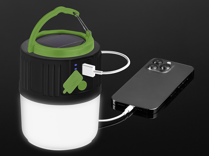 Latarnia solarna ładuje telefon za pomocą kabla USB. Latarnia ma zielony uchwyt. Telefon jest czarny.