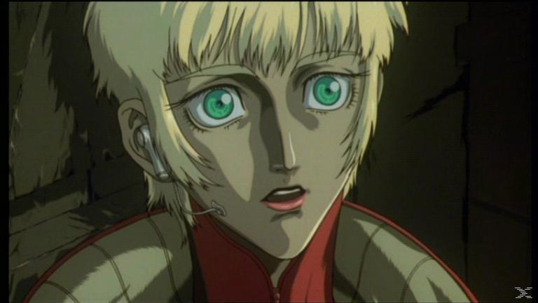 Anime-Figur mit grünen Augen, blonden Haaren und Headset. Trägt eine rot-grüne Uniform. Die Figur sieht überrascht aus.
