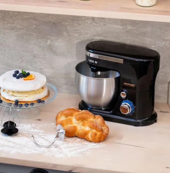 Czarny mikser, chałka, ciasto z jagodami i przybory kuchenne na blacie. Tło: półka.