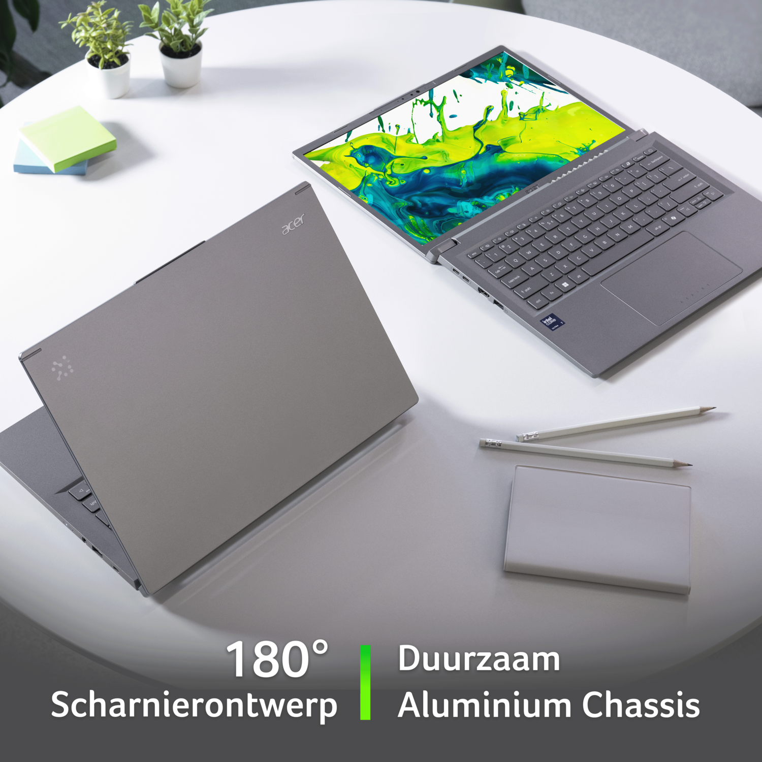 Twee Acer laptops op een witte tafel, één open, één dicht. Potloden, een wit blok en planten staan ook op de tafel.