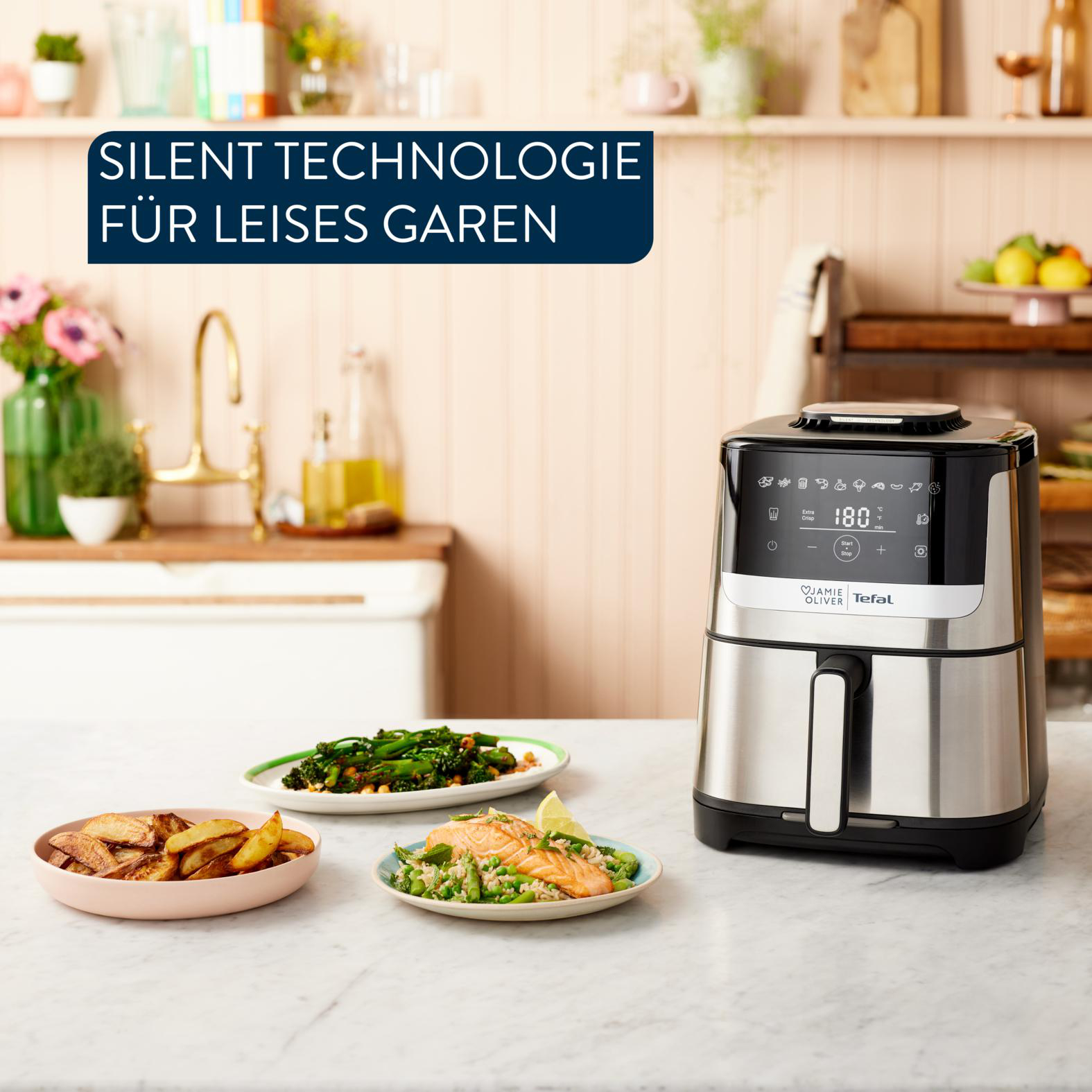 Ein Luftfritteuse mit Essensplatten und Text. Die Fritteuse ist aus Edelstahl. Teller halten Kartoffeln, Gemüse und Lachs.