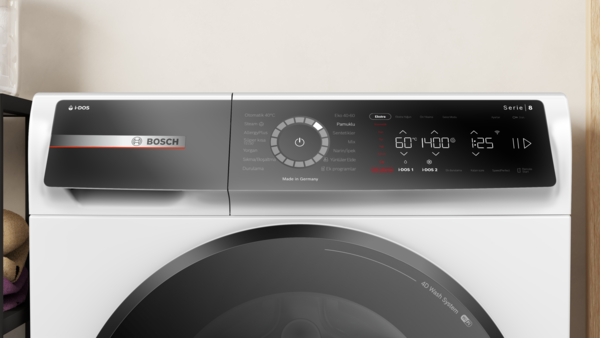 Beyaz bir Bosch çamaşır makinesi. Açma/kapama düğmesi ve dijital ekranlı siyah bir kontrol paneli vardır. Tambur görünür.