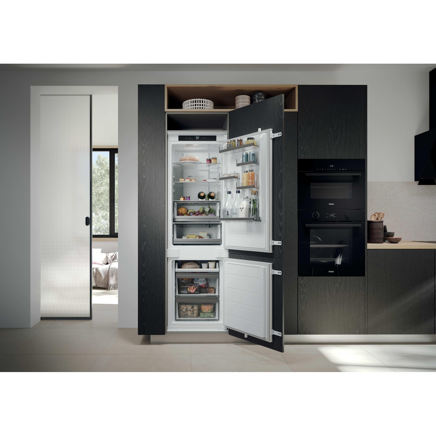 Cucina moderna con frigorifero parzialmente aperto pieno di cibo. Forno e armadi neri. Porta a vetri per il soggiorno.