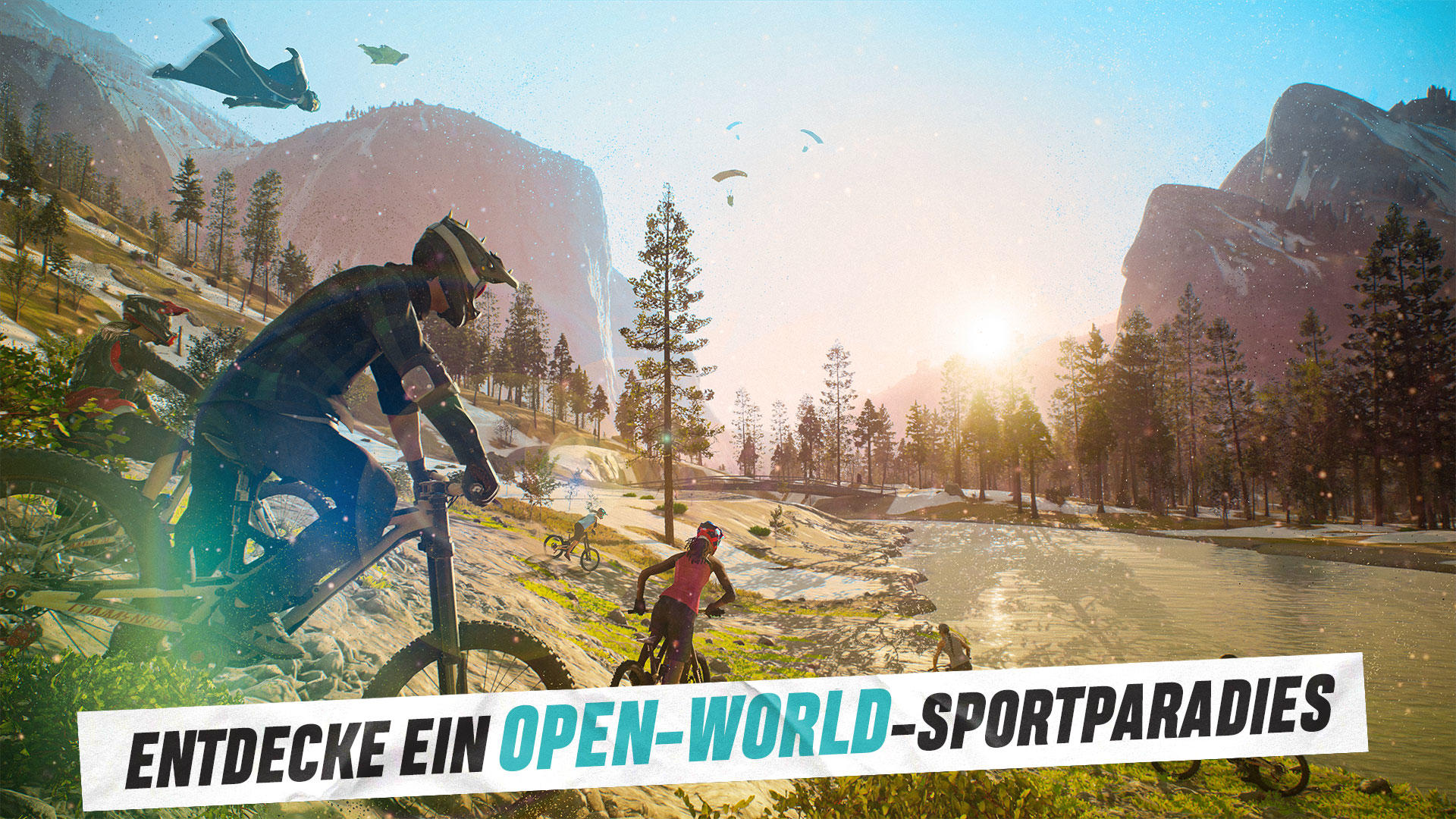 Mountainbiker fahren durch eine malerische Landschaft. Gleitschirmflieger und Wingsuits sind am Himmel. Berge und Bäume im Hintergrund.