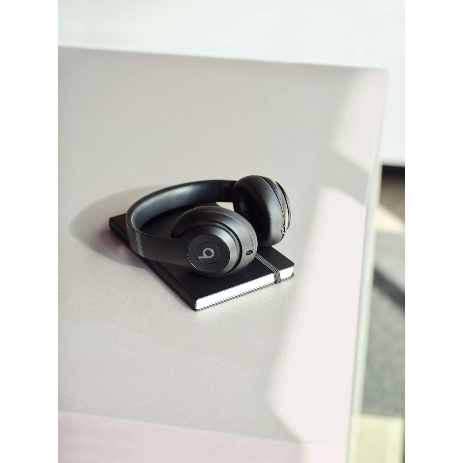 Cuffie nere su un taccuino nero chiuso su una superficie chiara. Il logo Beats è visibile sulle cuffie.