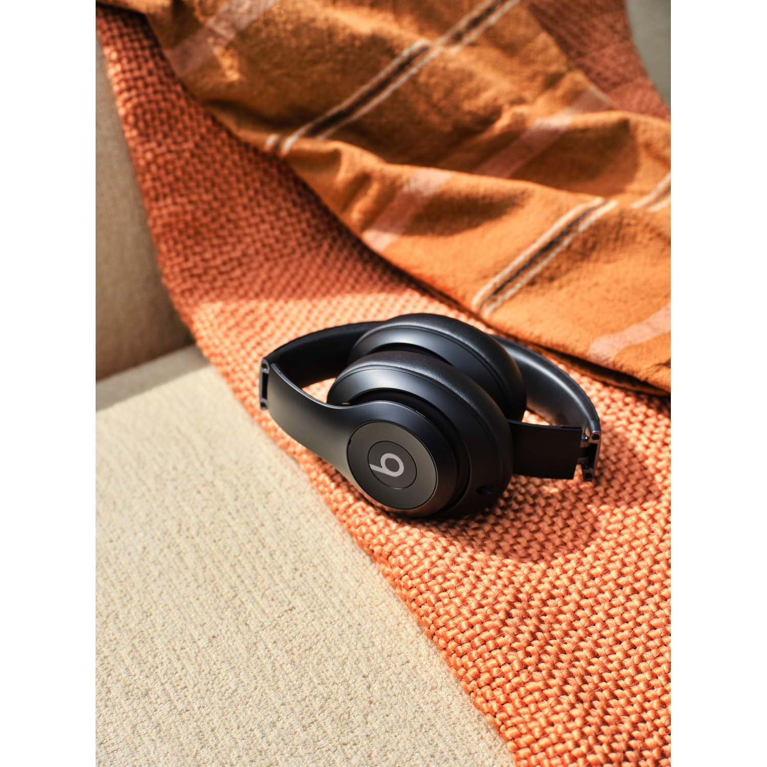 Cuffie Beats nere su una coperta arancione a maglia, superficie beige e coperta a quadri marrone.