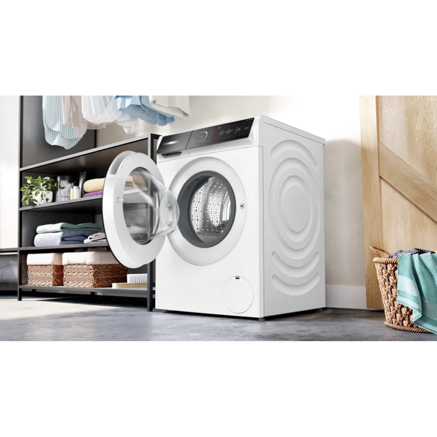 Een witte wasmachine met een open deur. Links planken met handdoeken en manden. Rechts een mand met een handdoek.