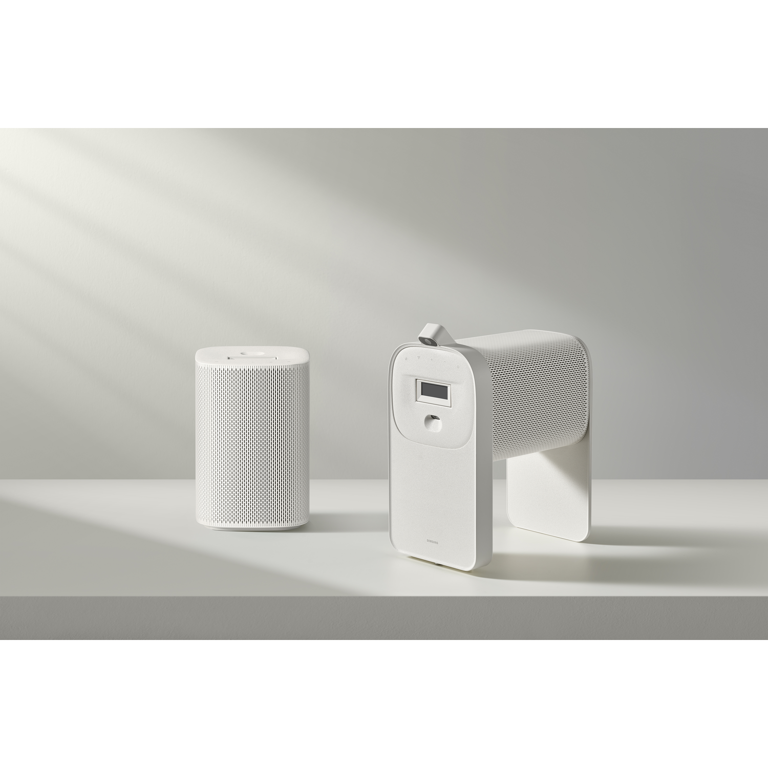 Deux enceintes blanches et modernes sur une surface blanche. L'une est cylindrique, l'autre a un écran et un design incurvé unique.