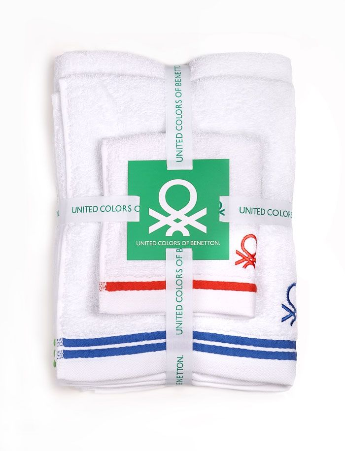 Fehér törölközőkészlet szalaggal átkötve, zöld címke középen. Piros és kék díszítések a törölközőkön. 'United Colors of Benetton'.