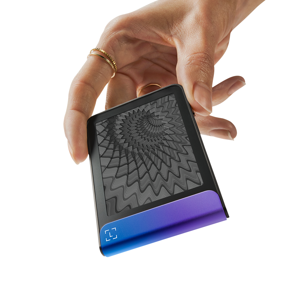 Una mano sostiene un dispositivo. El dispositivo tiene una pantalla negra con un patrón gris y una base degradada púrpura-azul.