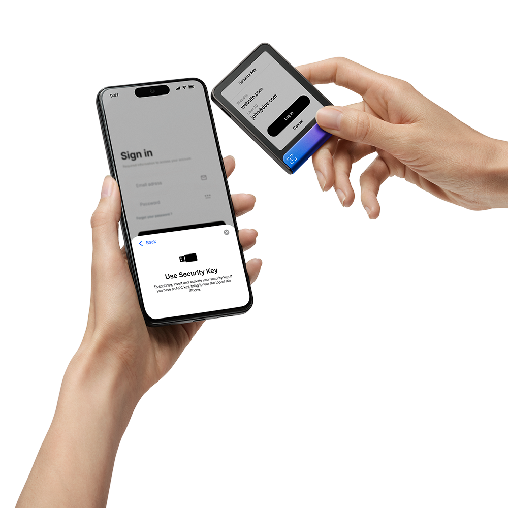 Manos sosteniendo un teléfono y una llave de seguridad. El teléfono muestra la pantalla de inicio de sesión, la llave muestra información de sitio web y usuario.