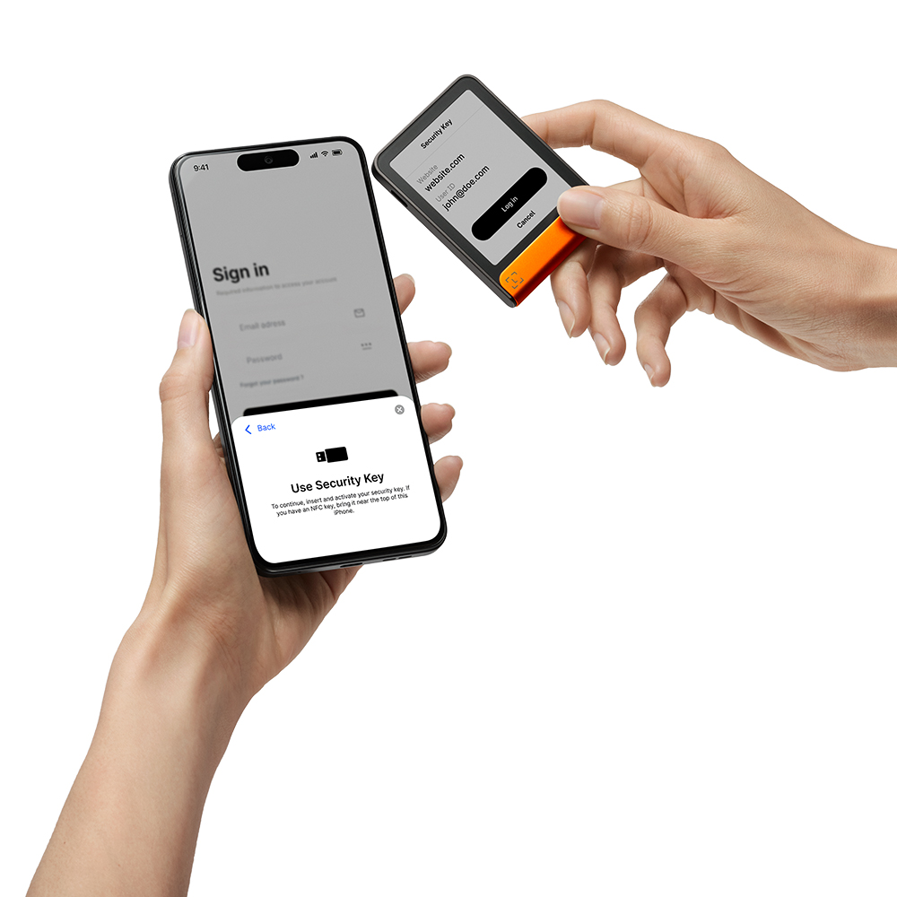Manos sosteniendo un smartphone y una llave de seguridad. El teléfono muestra la pantalla de inicio de sesión. La llave tiene información del sitio web y del ID de usuario.