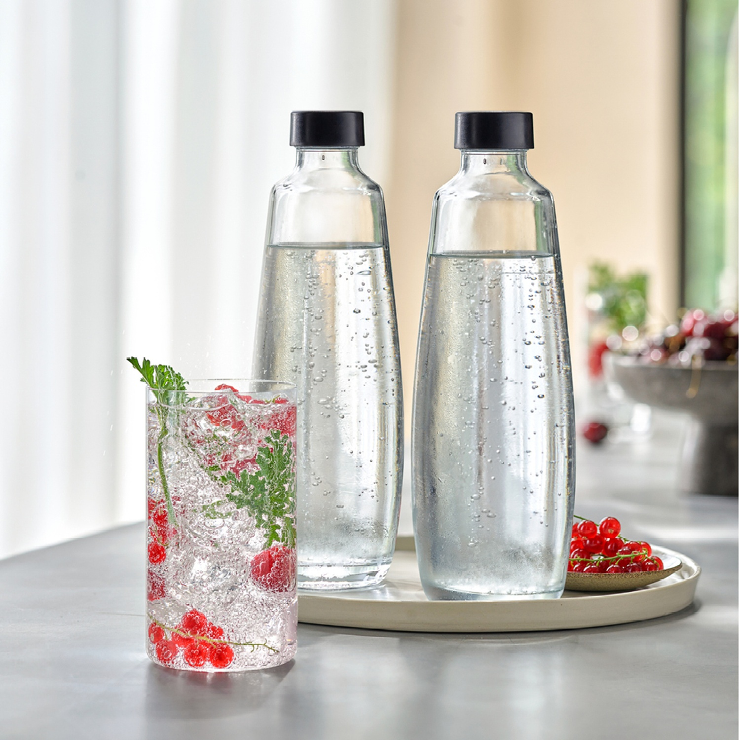 Due bottiglie d'acqua, un bicchiere d'acqua con frutti di bosco e menta e un piatto di frutti di bosco. Il tutto su un vassoio.