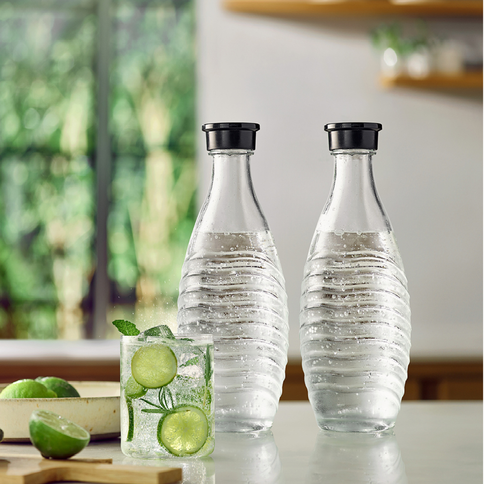 Due bottiglie d'acqua trasparenti con tappi neri, un cocktail con lime e menta e lime in una ciotola, tutto su un tavolo.