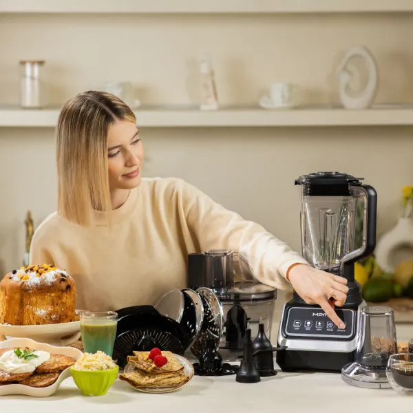 Kobieta obsługuje blender na stole z potrawami takimi jak naleśniki i ciasto. Widoczne są urządzenia kuchenne i składniki.