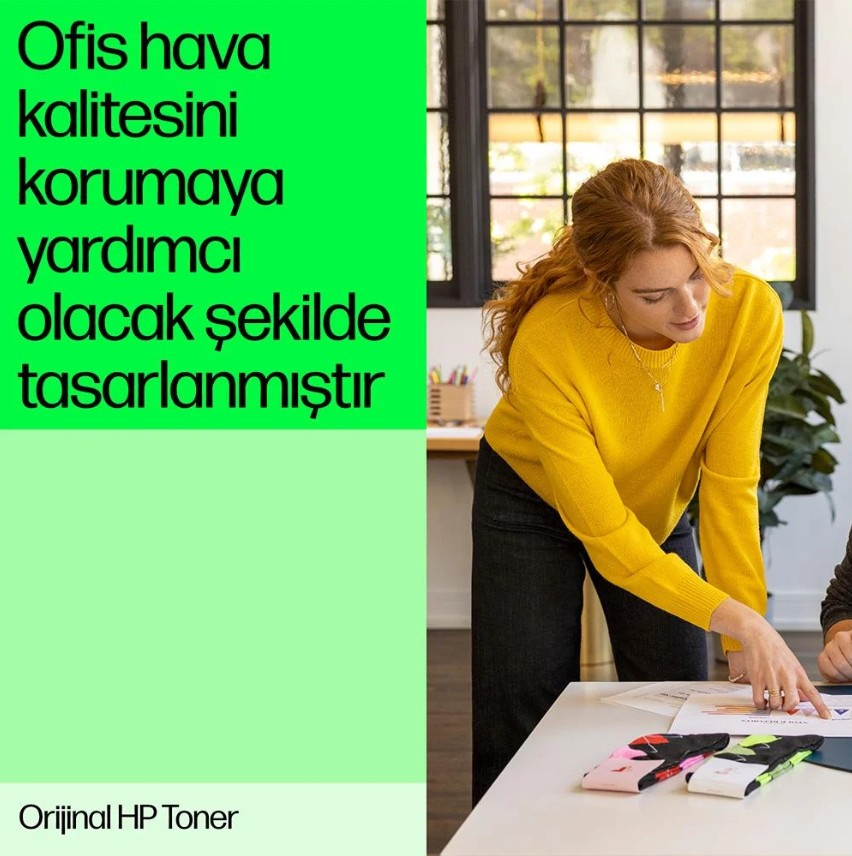 Sarı kazaklı kadın, masadaki bir kağıdı işaret ediyor. Renkli toner kutuları ve Türkçe metin görülüyor.