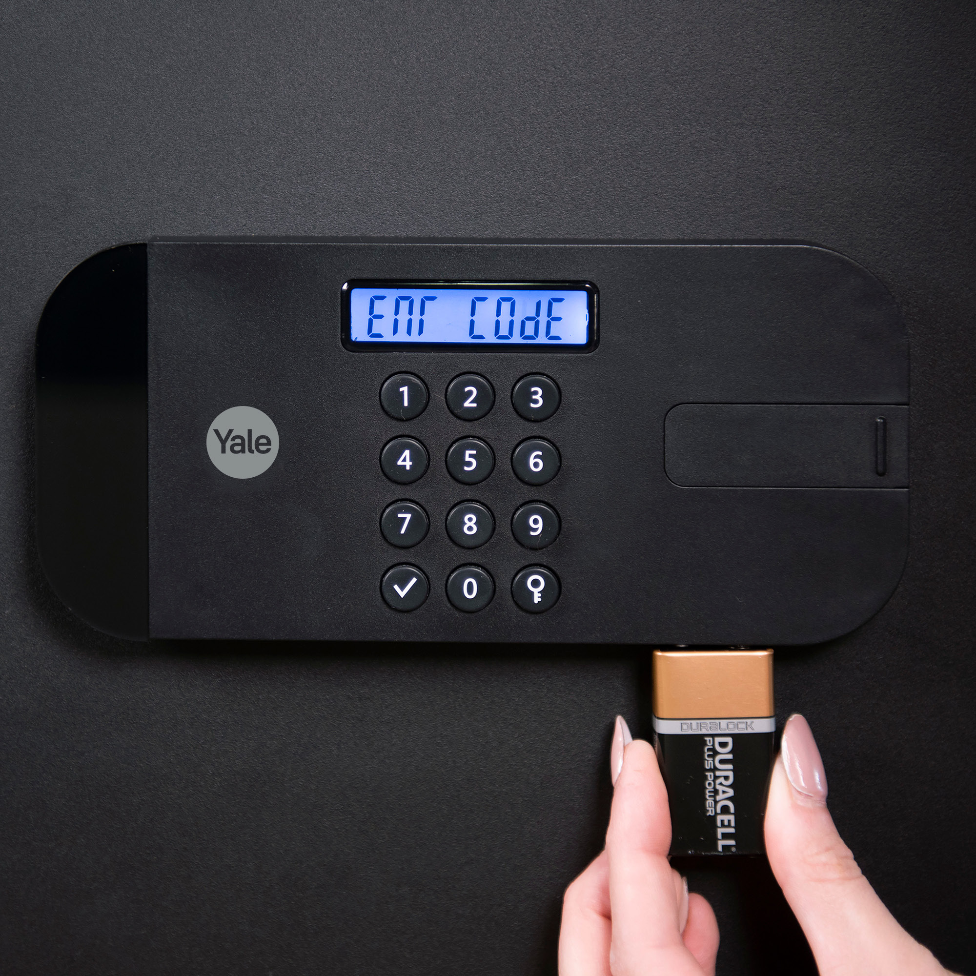 Eine Person steckt eine Duracell-Batterie in ein schwarzes Tastenfeld mit Digitalanzeige 'ENT CODE'.