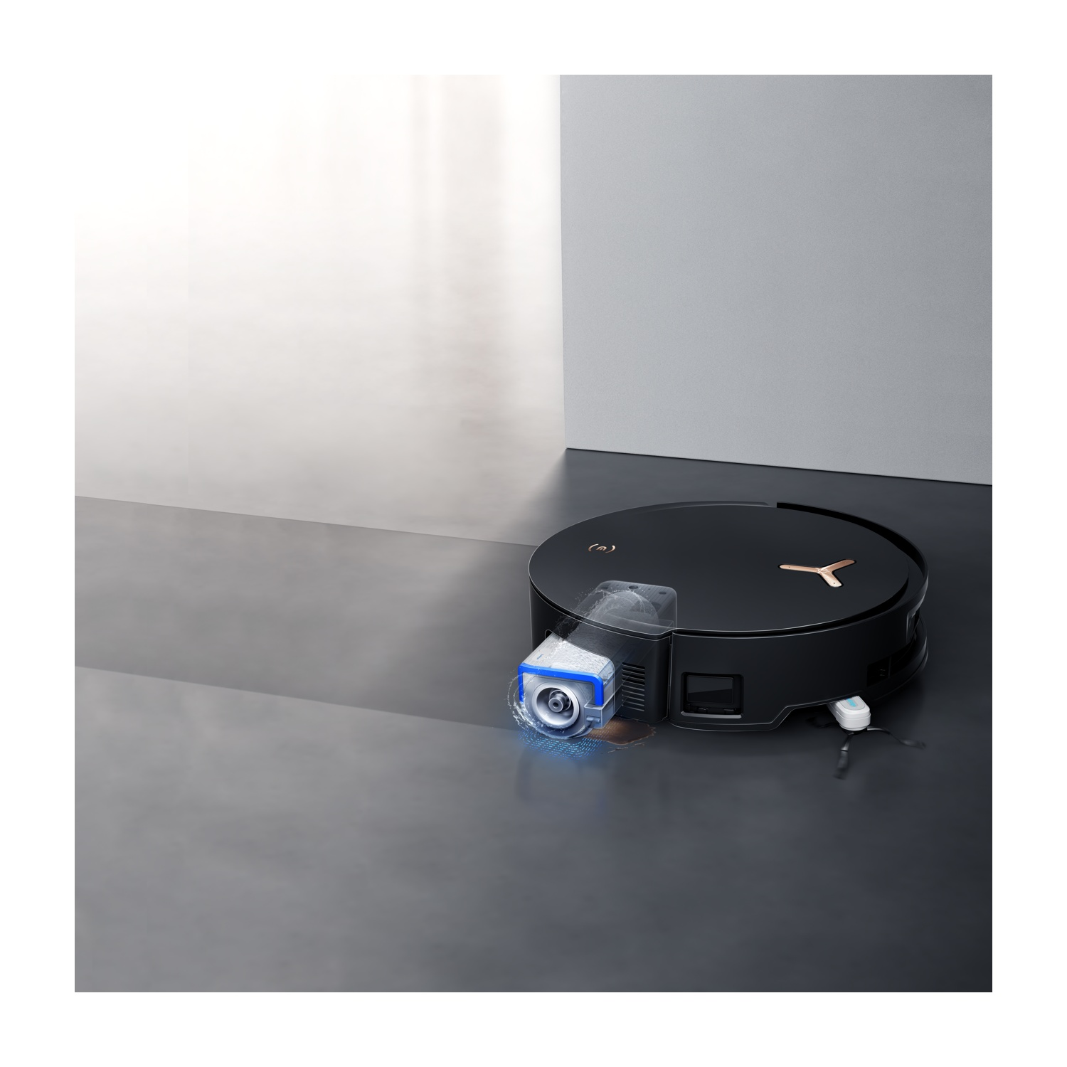 Un aspirapolvere robotico nero su un pavimento grigio. Ha un serbatoio dell'acqua blu e trasparente. Lo sfondo è un muro bianco e grigio.
