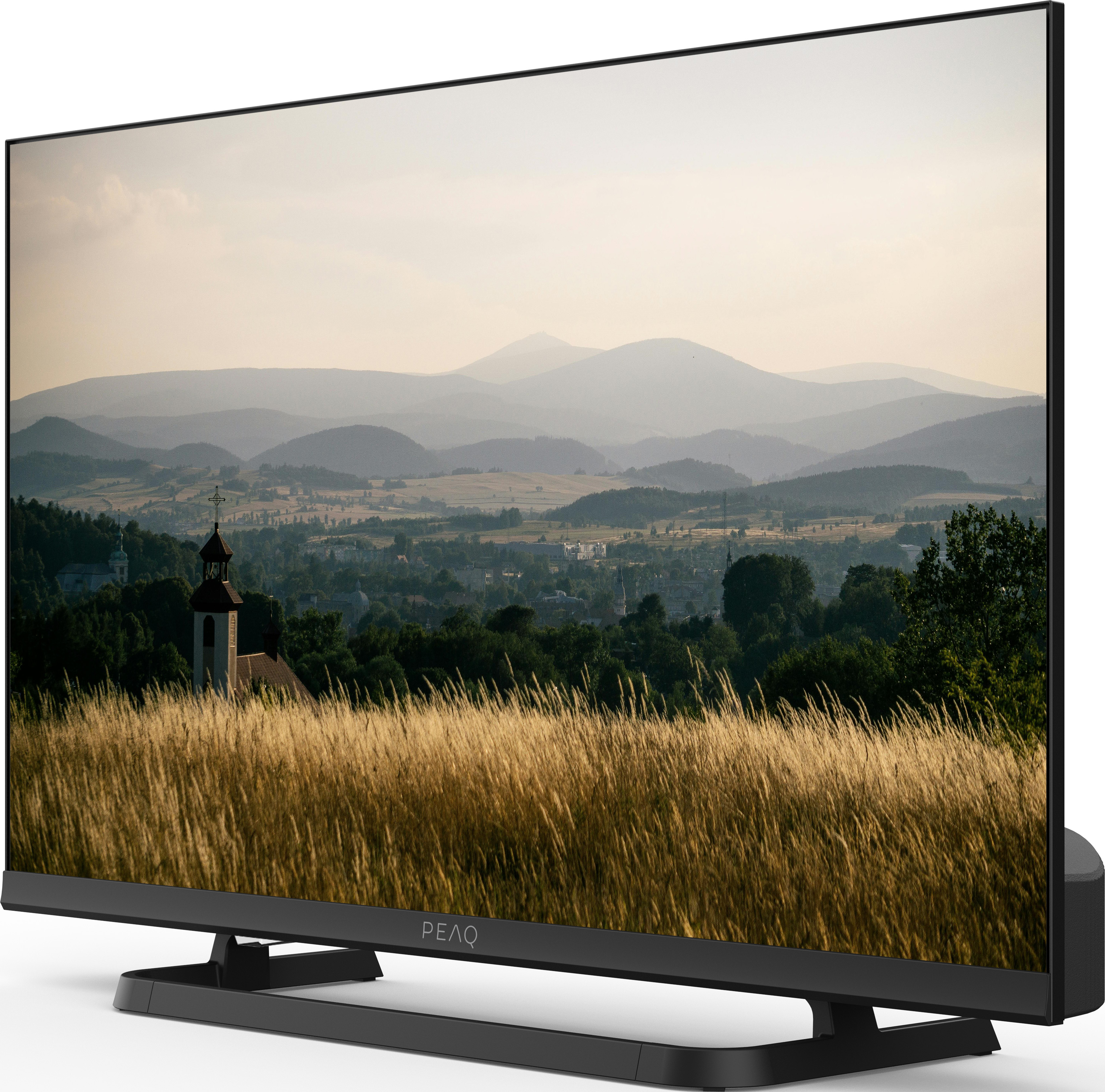 Ein Fernseher zeigt eine malerische Landschaft. Im Vordergrund ein Feld. Berge und eine Stadt im Hintergrund.