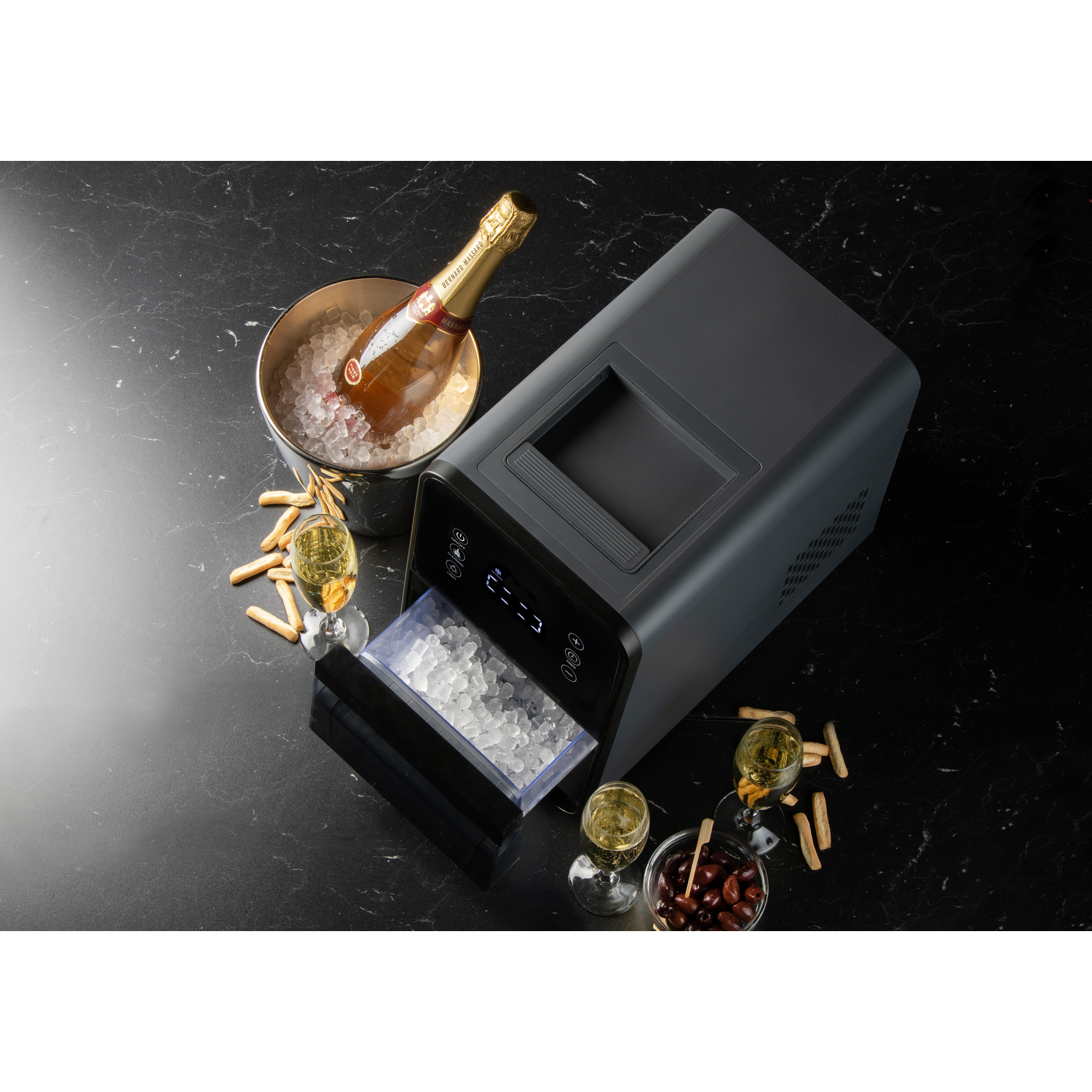 An ice machine with champagne, glasses, and olives on a black marble surface.