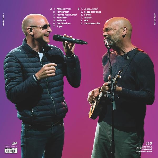 Zwei Männer singen und spielen Musik vor einem violetten Hintergrund.
